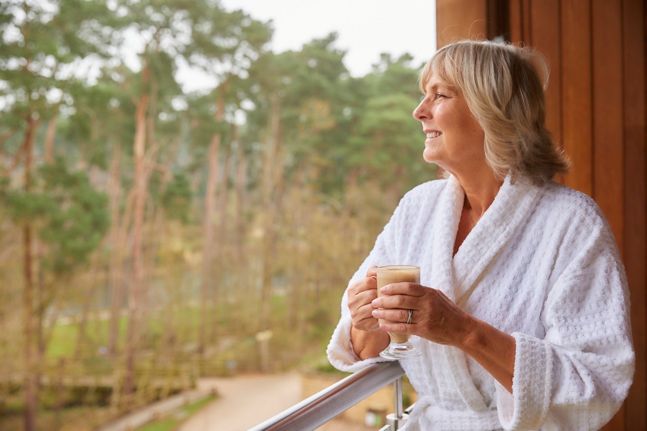 Woman drinking a coffee whilst looking out to the forest